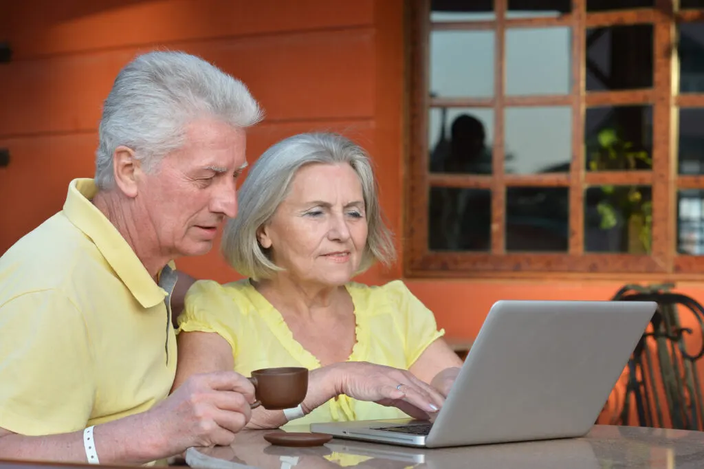Elder Couple in Yellow Shirts Looking at Silver Computer