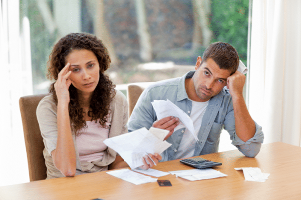 Stressed couple dressed in light brown and denim shirts sitting at table holding up estate planning and tax documents